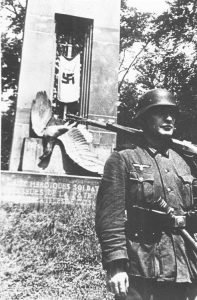 While French diplomats try to negotiate a better surrender, a Wehrmacht soldier stands guard over the Compiègne war memorial, the German eagle stabbed with the French sword: now enlivened by a Nazi flag.