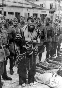 Wehrmacht soldiers now in town of Olkusz, in Nazi-occupied Poland; all males aged 14 & over made to lie face-down in town square for "registration".As registration begins, local Rabbi Moshe Hagermann has been ordered to pray, barefoot, for amusement of German soldiers