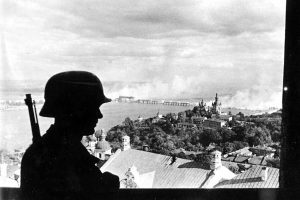 With a burning bridge across the Dnieper river in the background, a German sentry keeps watch in the recently-captured city of Kiev, in 1941